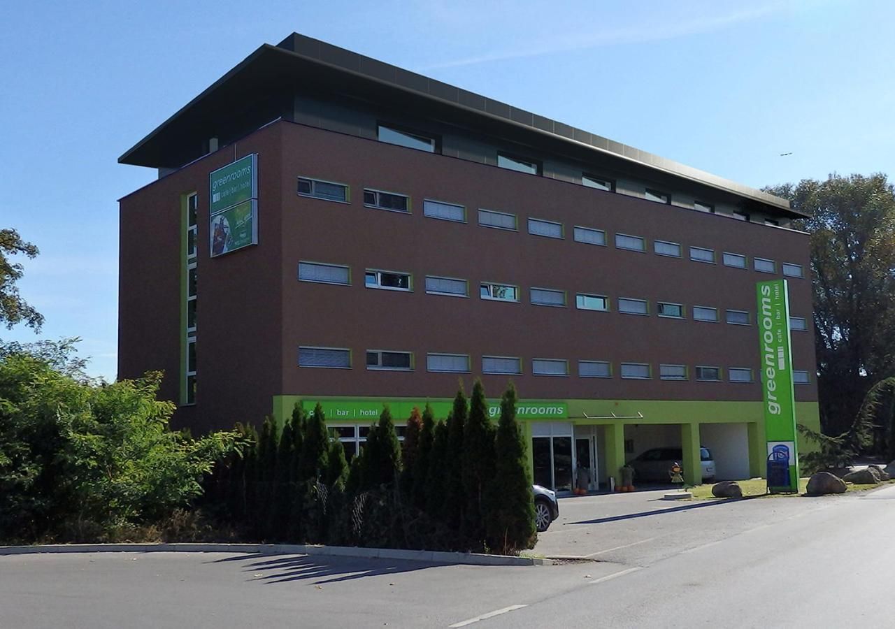 A multi-story building with a green and brown facade, a visible entrance, and a parking area.