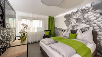 Moderni hotellihuone, jossa on suuri sänky, työpöytä maljakko täynnä kukkia ja seinälle asennettu televisio.
