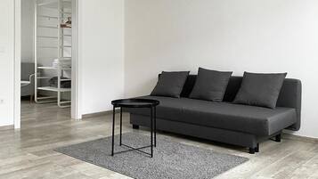 Een moderne woonkamer met een grijze bank, een klein zwart bijzettafeltje en een grijze vloerkleden.