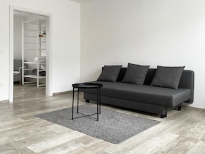 Un salon moderne avec un canapé gris, une petite table d’appoint noire et un tapis gris.