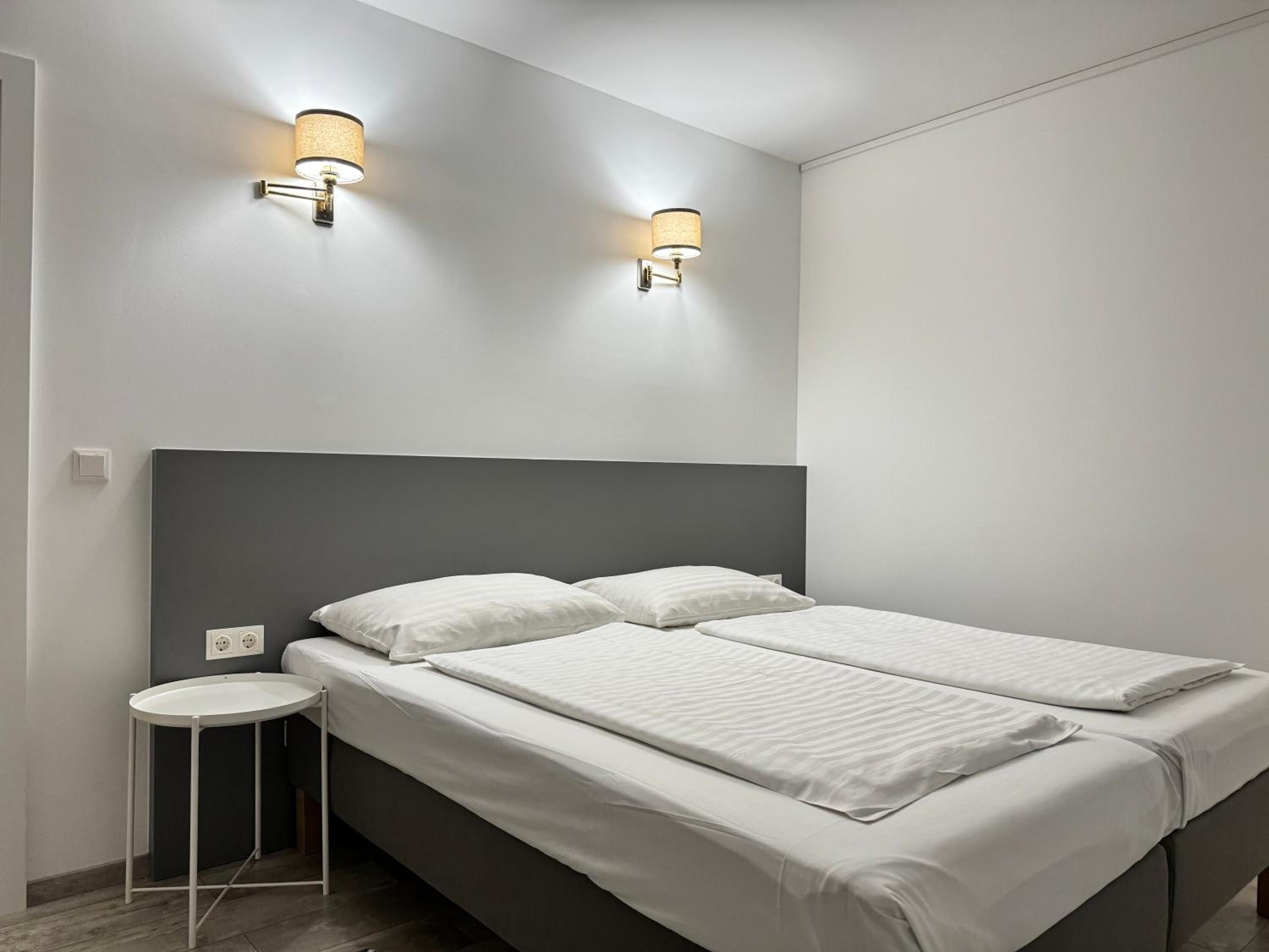 A modern bedroom with a double bed, two wall-mounted light fixtures, and a small bedside table.