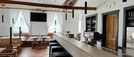 A restaurant with a long counter, bar stools, and a clock on the wall.