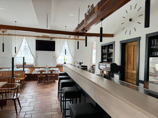 A restaurant with a long counter, bar stools, and a clock on the wall.