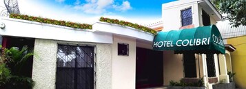 Un hotel llamado 'Hotel Colibri' con toldo verde, fachada blanca y una ventana con reja de metal.