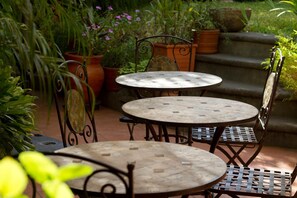 A patio area with two round tables and metal chairs, surrounded by potted plants and steps leading to a garden area. - Hotel y Desayuno Colibri (Managua)
