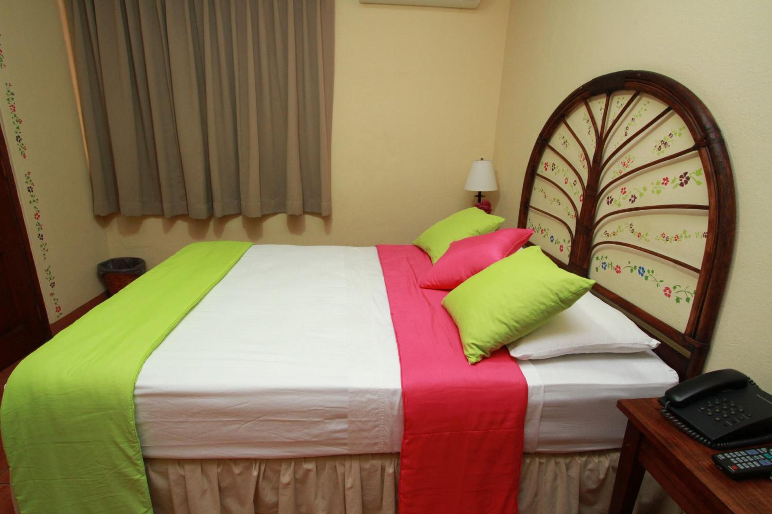 A neatly made bed with a white and red bedspread, a green pillow, and a wooden headboard with floral patterns.