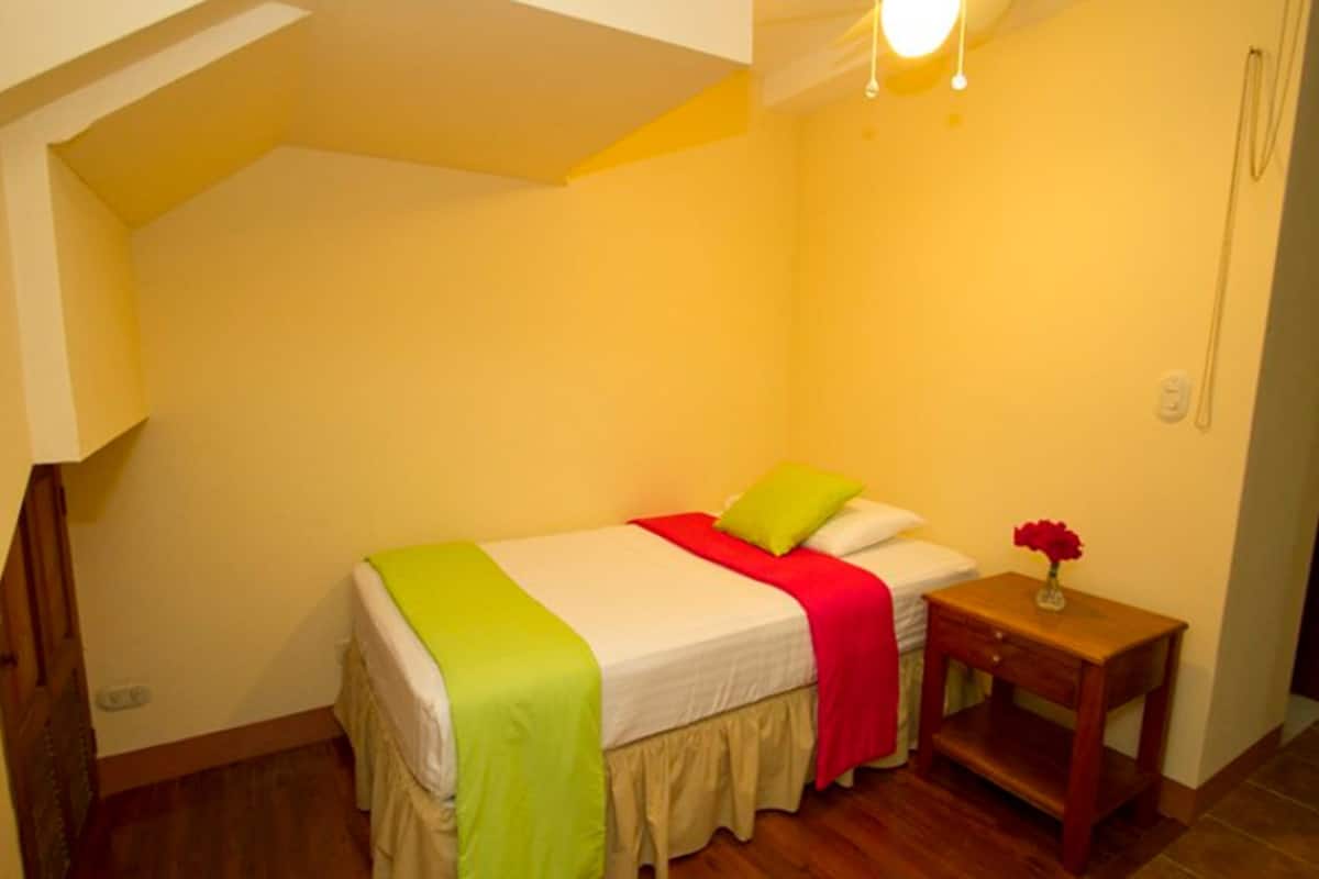 A small, neatly arranged bedroom with a single bed, a nightstand, and a bedside table.