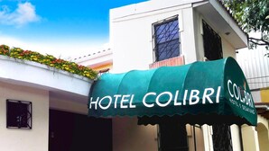 A hotel named 'Hotel Colibri' with a green awning and a flower bed above the entrance. - Hotel y Desayuno Colibri (Managua)