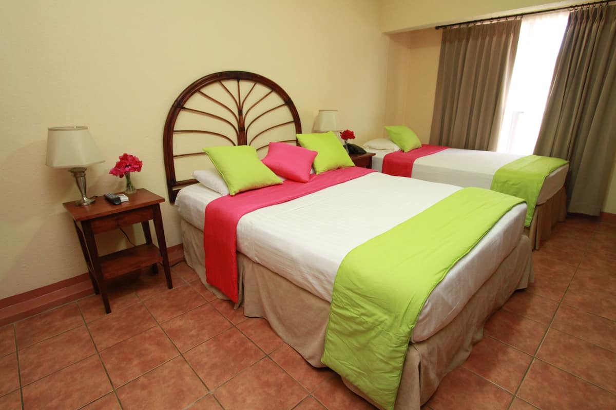 A hotel room with two beds, each with a wooden headboard, a nightstand with a lamp, and a vase with flowers.