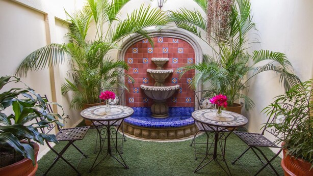 A courtyard with a tiled fountain, two round tables with chairs, and potted plants. - Hotel y Desayuno Colibri (Managua)