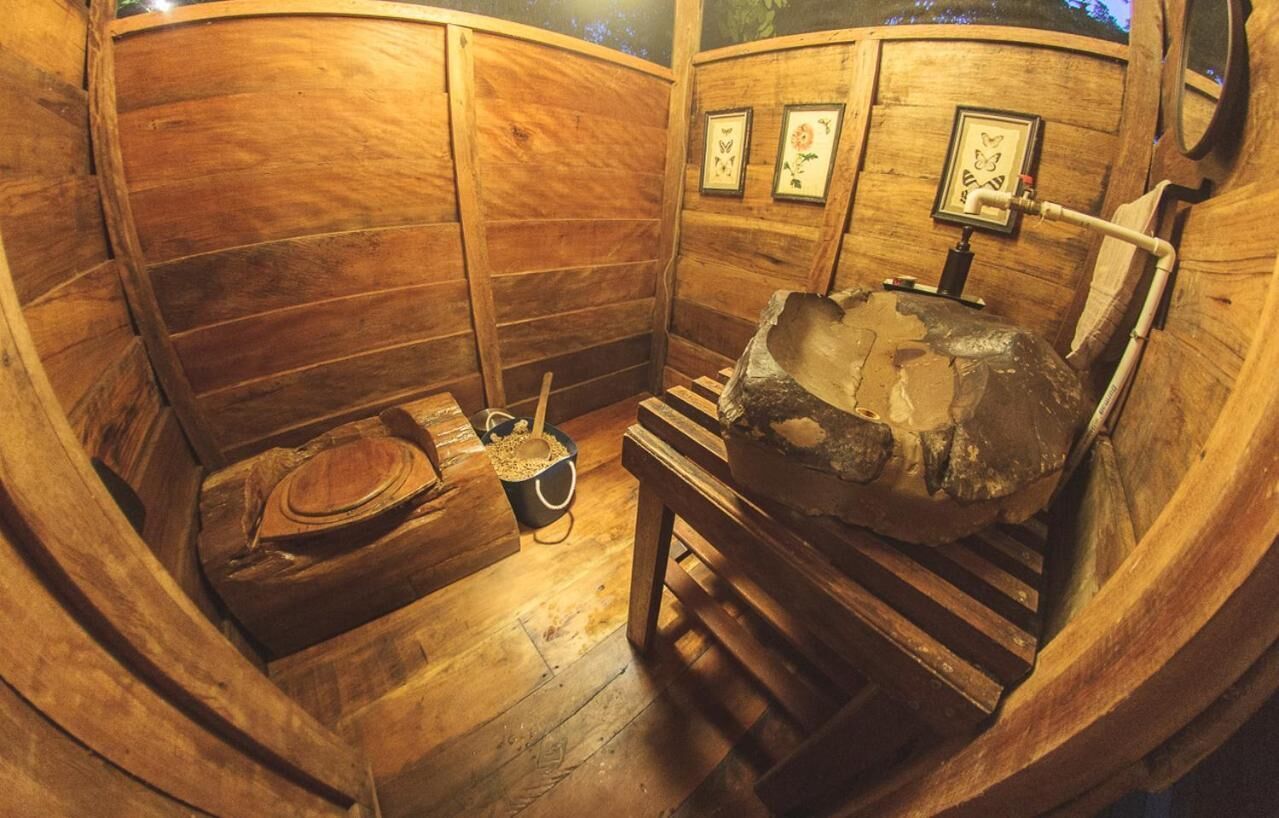 A wooden cabin interior with a rustic wooden bench, a small table with a bowl, and framed pictures on the wall.