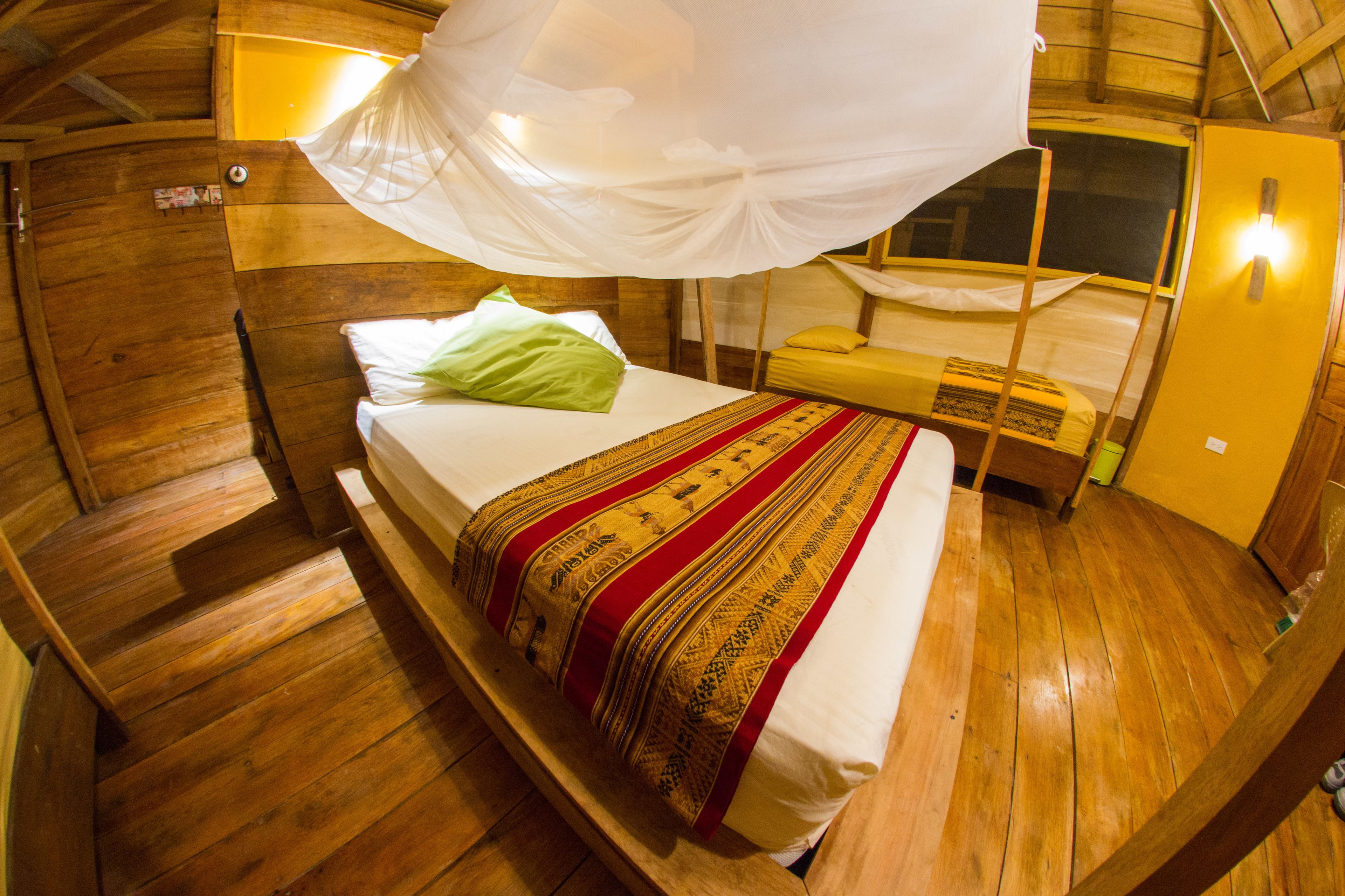Quarto de madeira com cama, um banco e mosquiteiro.