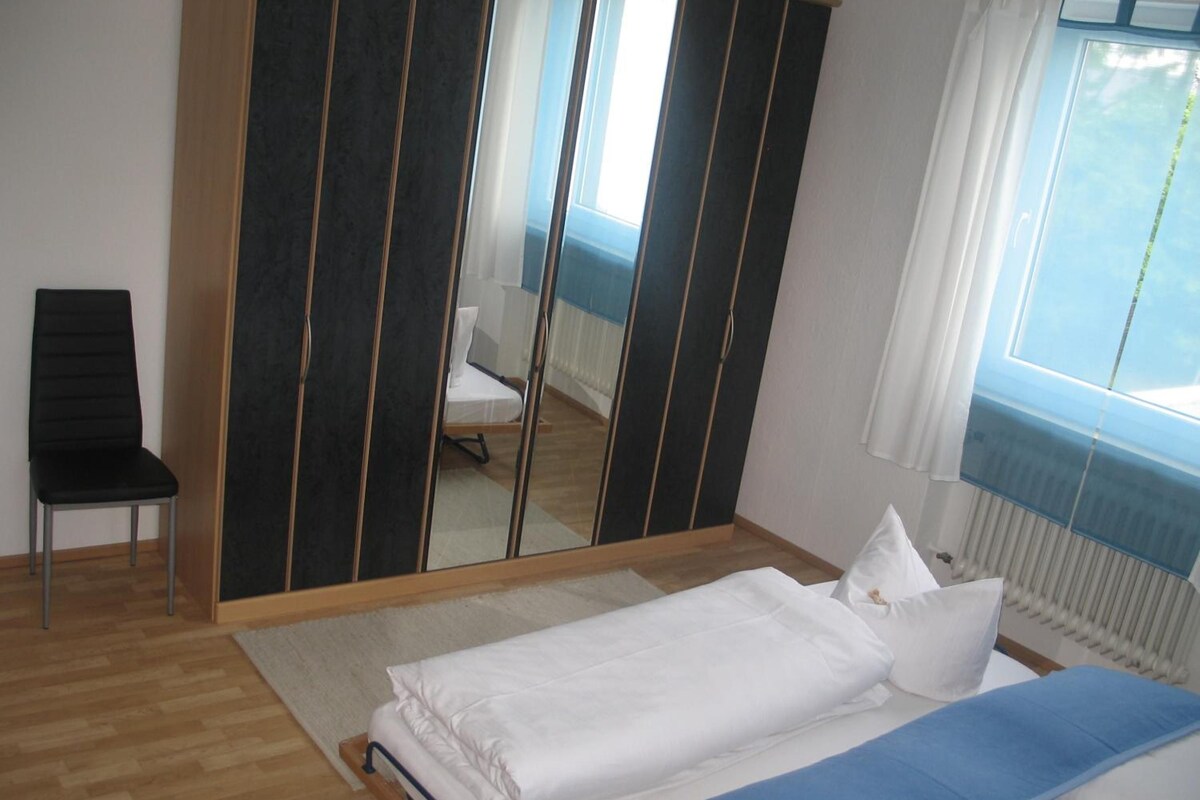 A bedroom with a bed, a chair, a mirror, and a window.