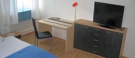 Una habitación de hotel con una cama, un escritorio con computadora, una televisión y una silla.