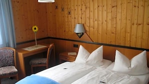 Et hotelværelse med træpaneler, en seng med hvide sengetøj, et skrivebord med stol og en lampe.