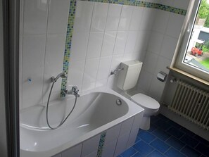 A bathroom with a bathtub, toilet, and a window.