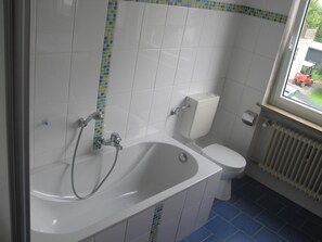 A bathroom with a bathtub, toilet, and a window.