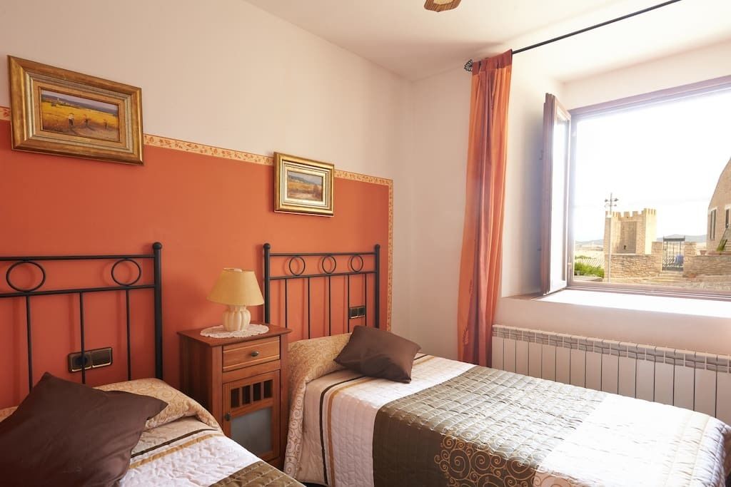A bedroom with two beds, a window with a view of a castle, and a radiator.