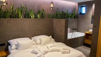 A modern hotel room with a large bed, a ceiling fan, a bathtub, and a small window.