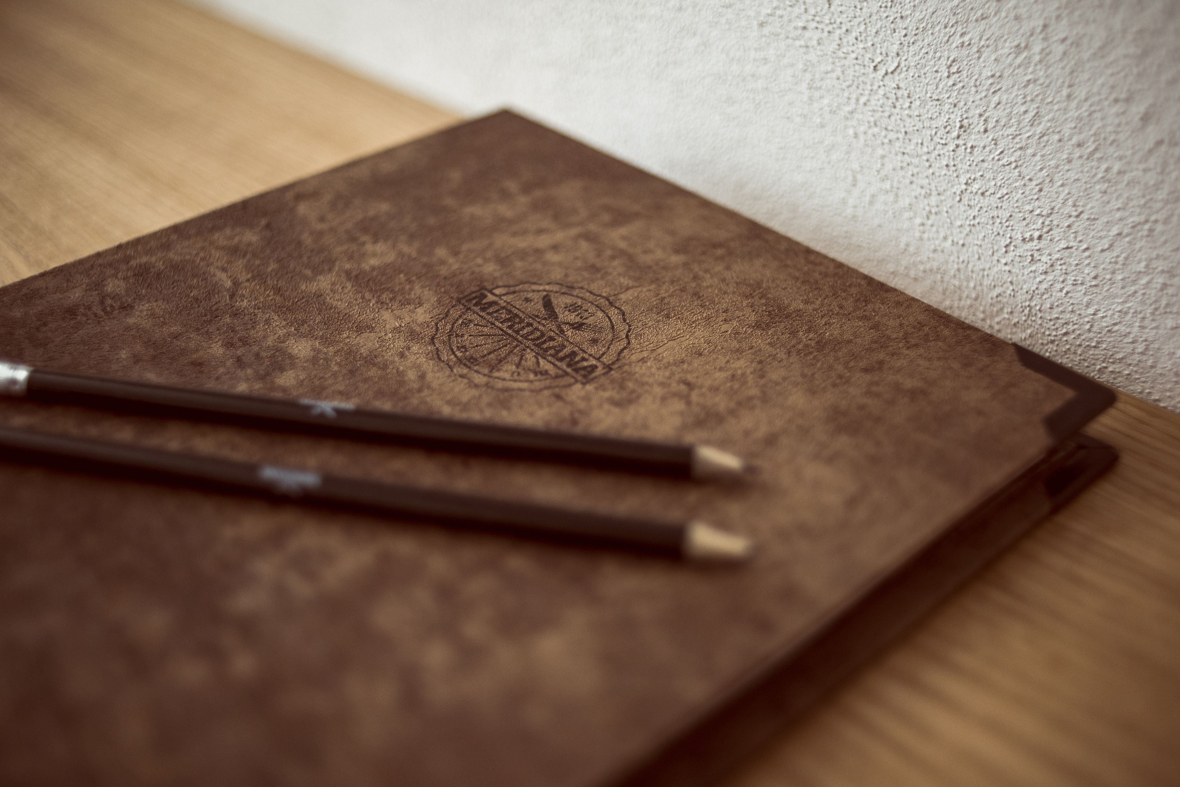 A brown leather-bound notebook with a circular embossed logo on the cover, placed on a wooden surface.
