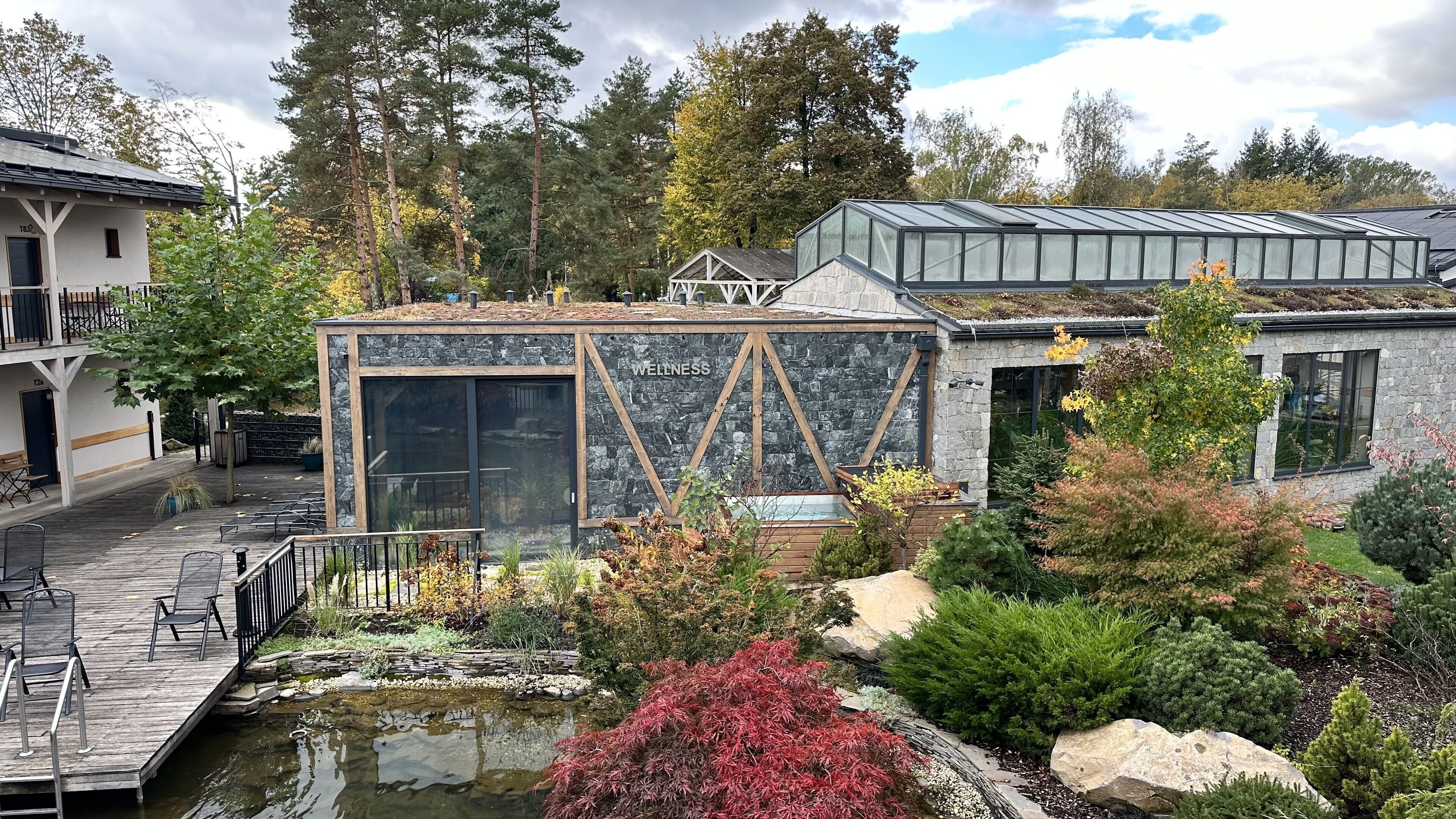 A modern building with a large glass facade, a stone exterior, and a well-maintained garden with a pond and various plants.