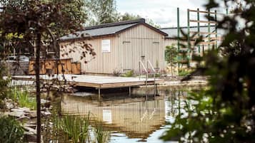 A wooden shed with a dock over a pond, surrounded by greenery and trees.