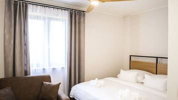 Una habitación de hotel con cama, una silla, ventilador de techo y ventana con cortinas.
