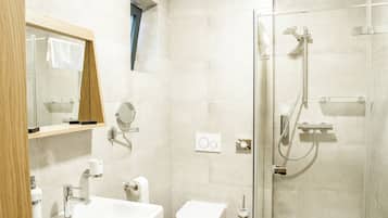 Ein modernes Badezimmer mit einer gläsernen Dusche, einem Holzkosmetikschrank mit Spiegel, einer Toilette und einem Waschbecken.