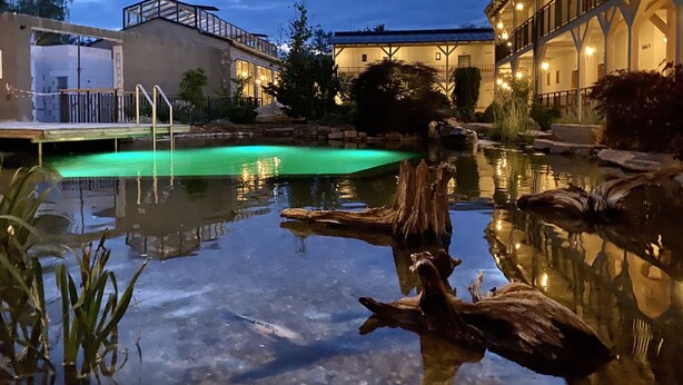 Una piscina con cubierta de madera y un edificio con balcón al fondo.