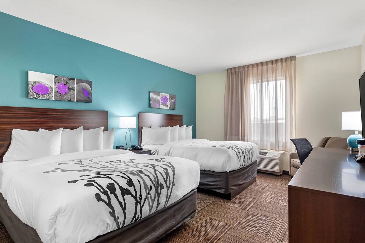 A hotel room with two beds, a desk, a chair, and a window with curtains.