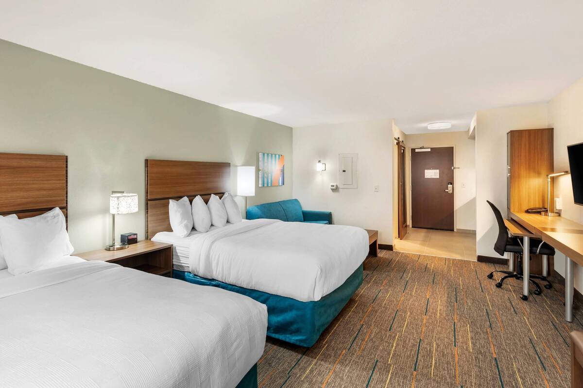 A hotel room with two beds, a desk, a chair, a lamp, and a television.