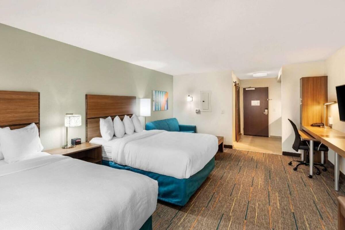 A hotel room with two beds, a desk, a chair, a TV, and a door leading to another room.