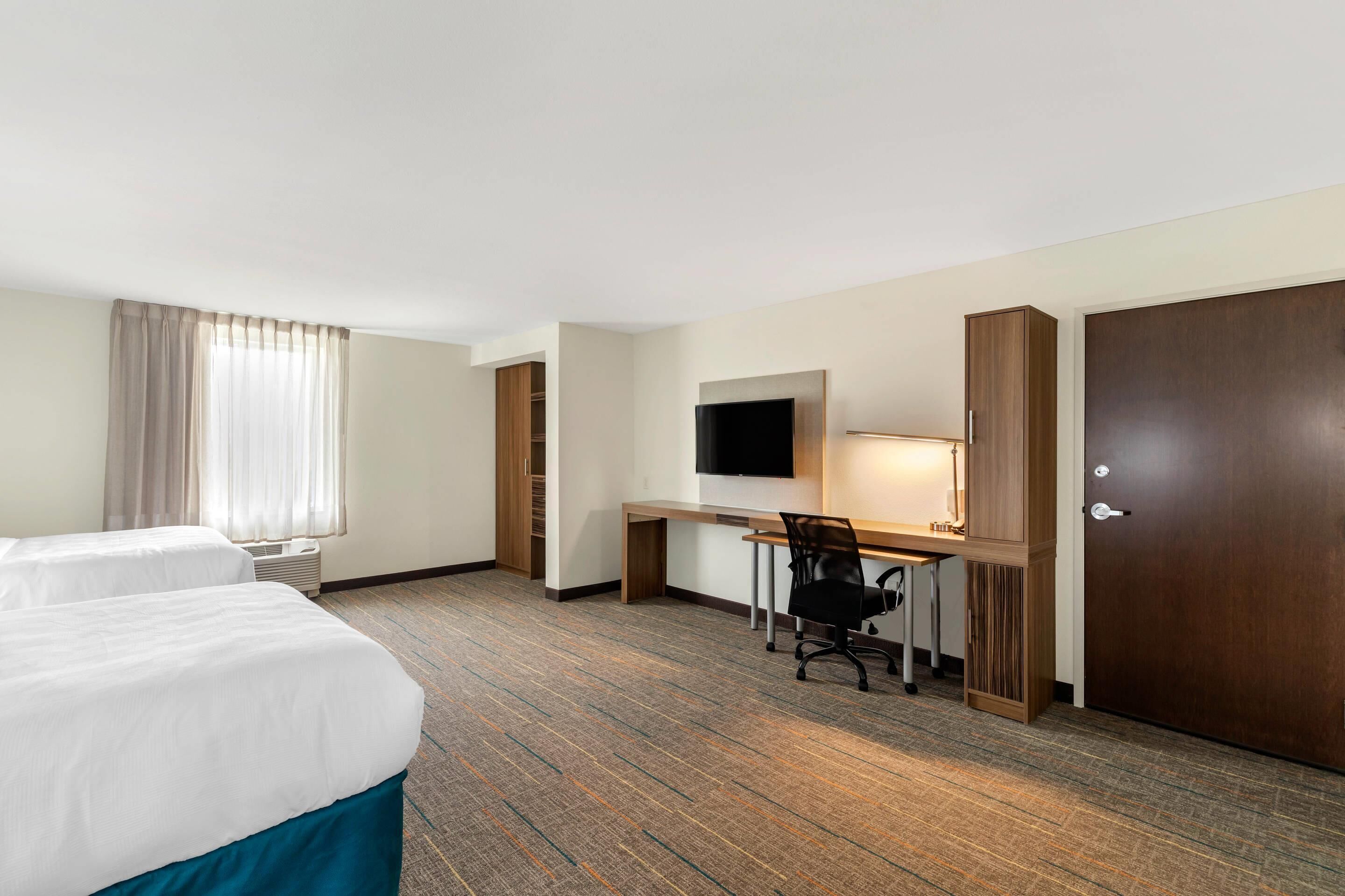 Ein Hotelzimmer mit zwei Betten, einem Schreibtisch mit Stuhl, einem Fernseher und einem Kleiderschrank.