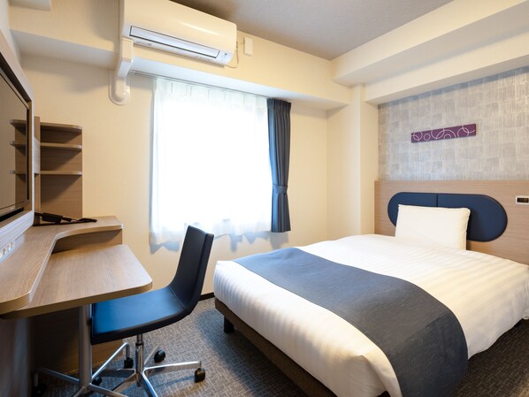 Habitación de hotel con cama, escritorio, silla y aire acondicionado.