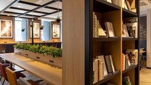 A modern library with wooden bookshelves, a long table with chairs, and hanging plants. - Comfort Hotel Shin-Osaka (Osaka)