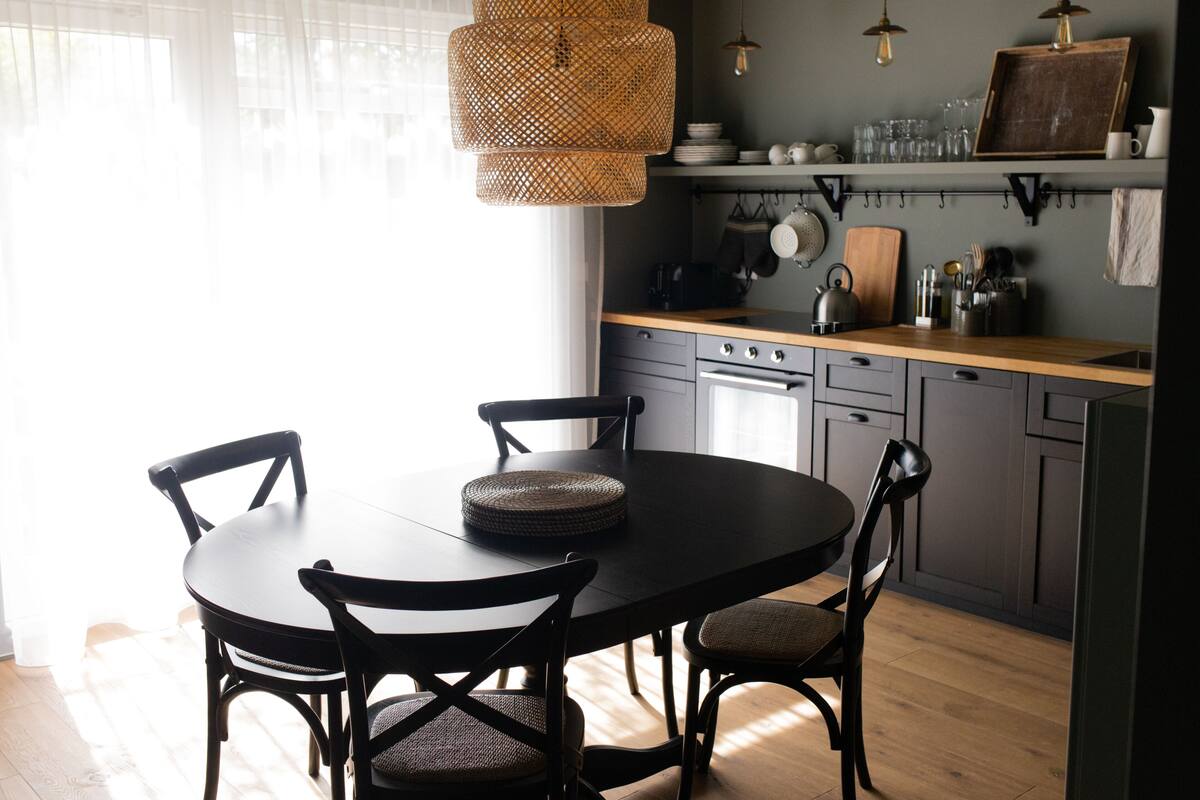 A modern kitchen with a round dining table, chairs, and a hanging light fixture.