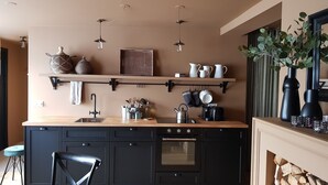 A modern kitchen with black cabinets, a wooden countertop, a built-in oven, and a hanging pot rack.