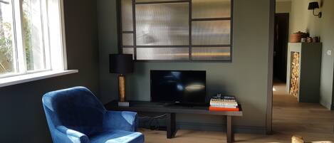 Een woonkamer met een blauwe fauteuil, een flatscreen televisie, een houten salontafel en een boekenplank.