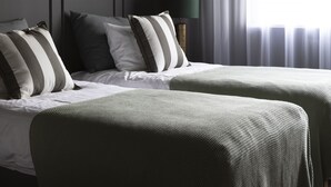 A bedroom with two beds, a hanging light fixture, a bedside lamp, and sheer curtains.