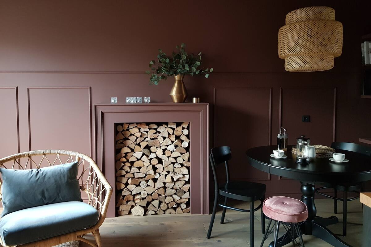 A cozy room with a fireplace, a wicker chair, a round table with chairs, and a hanging light fixture.