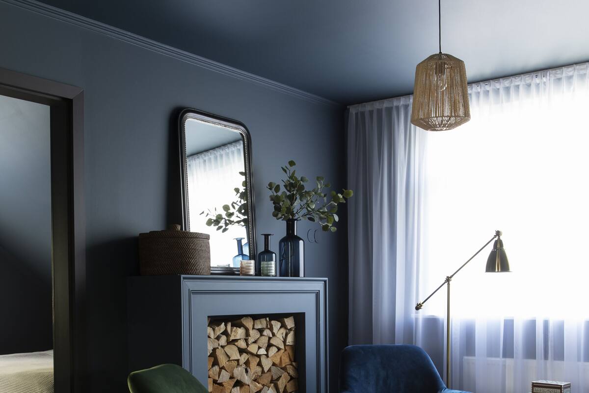 A modern living room with a fireplace, a green armchair, a blue armchair, and a floor lamp.