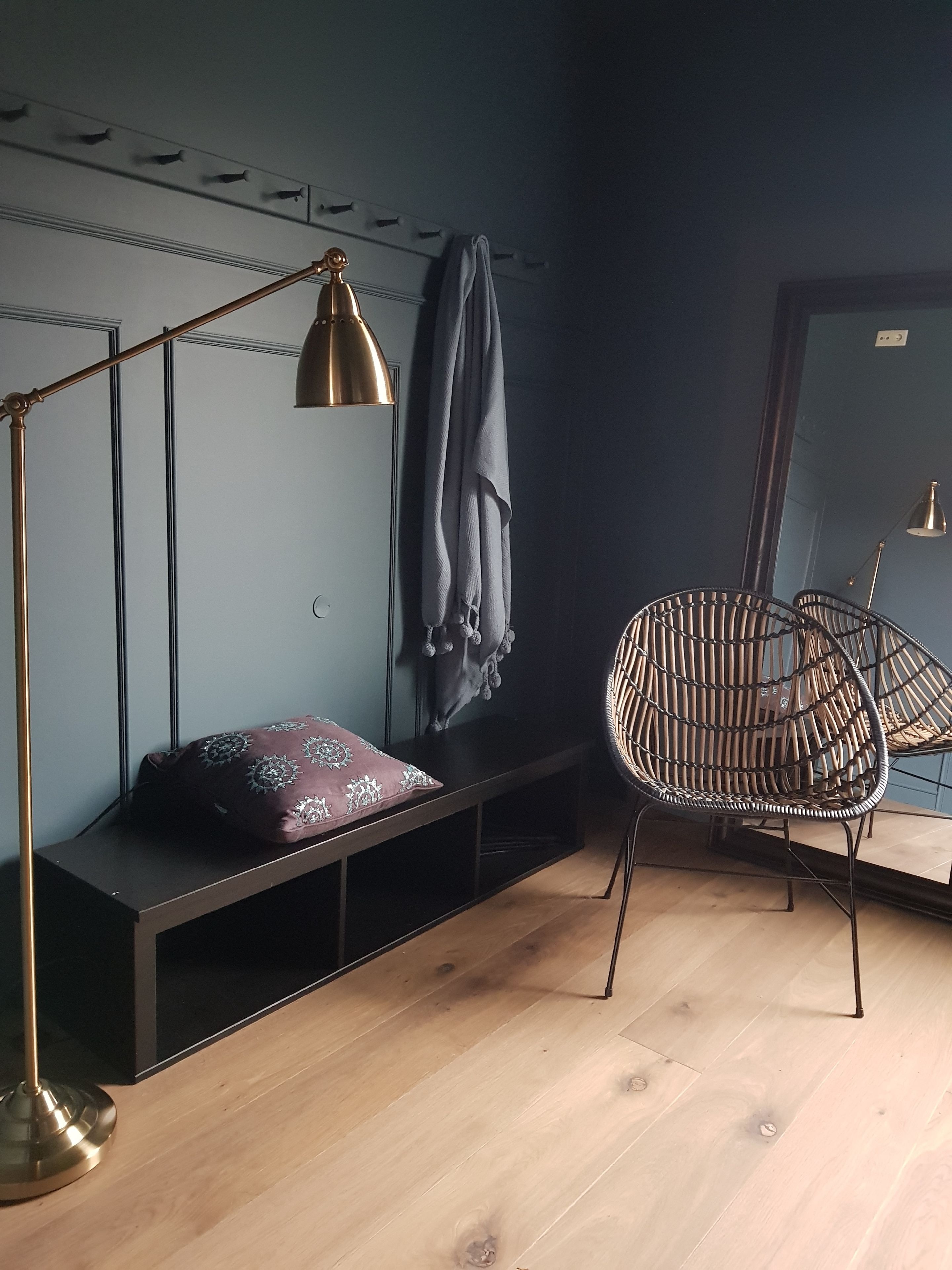 A room with a bench, a rattan chair, a floor lamp, and a hanging towel.