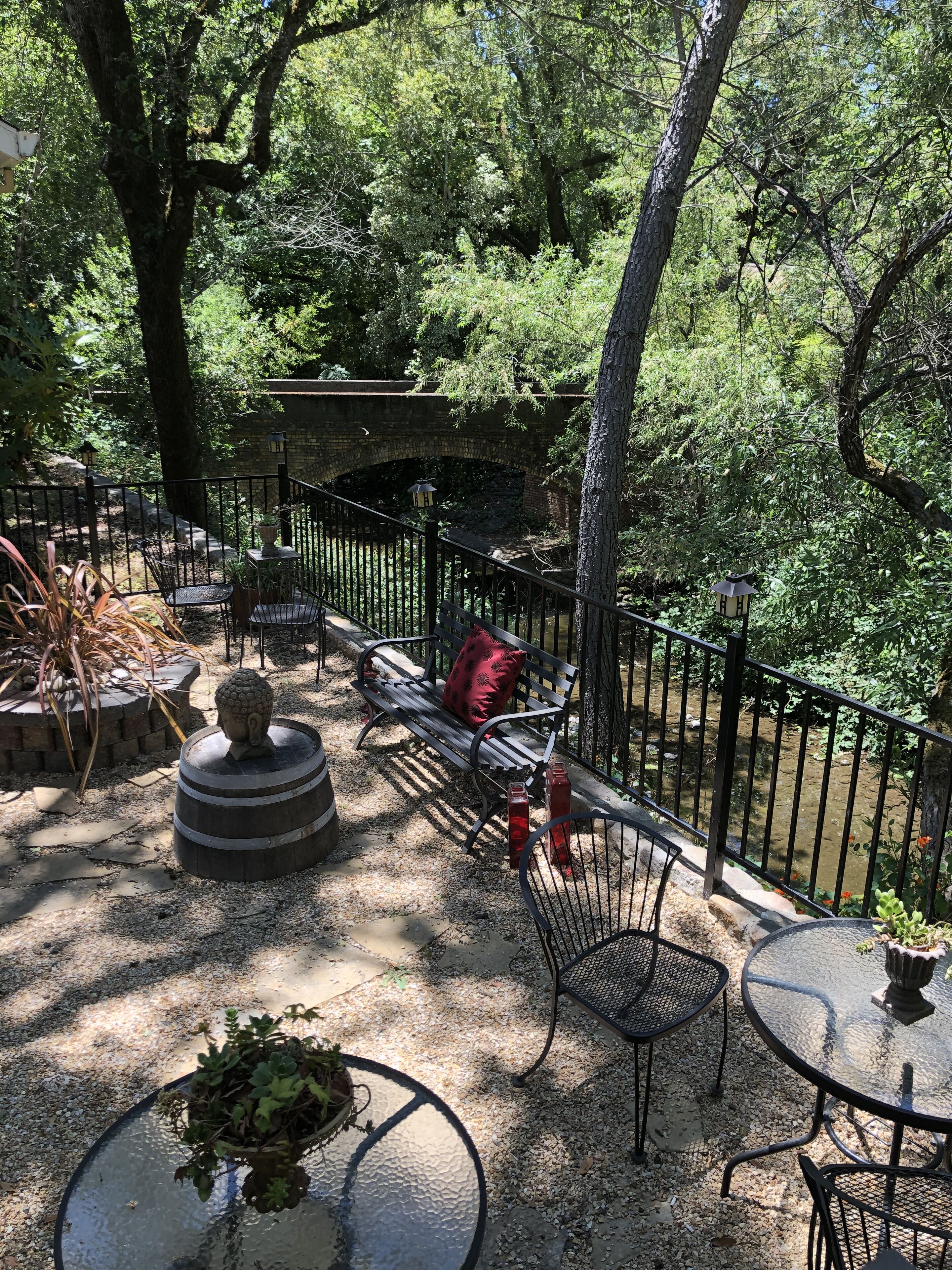 An outdoor patio area with a stone bench, a round table with a plant, and a metal fence.