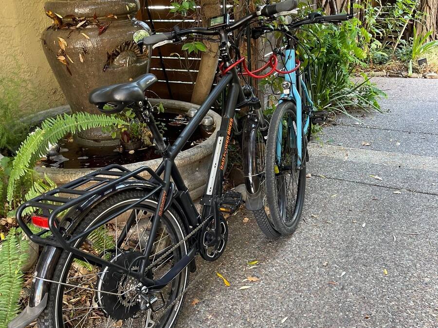 Un vélo est garé à côté d’une fontaine en pierre, dans un jardin verdoyant, délimité par une clôture en bois.