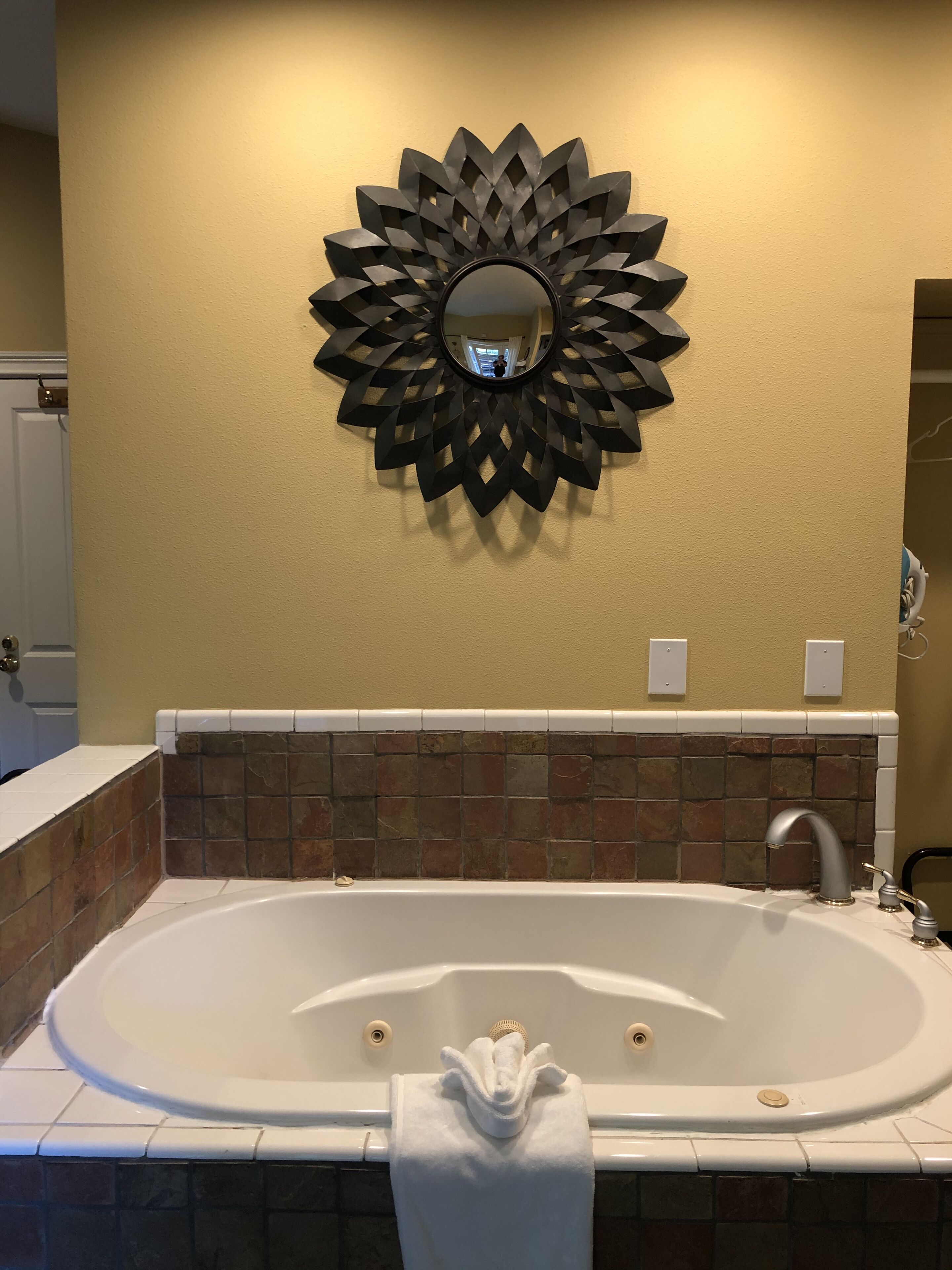 A bathroom with a freestanding bathtub, a decorative wall mirror, and a towel on the edge.