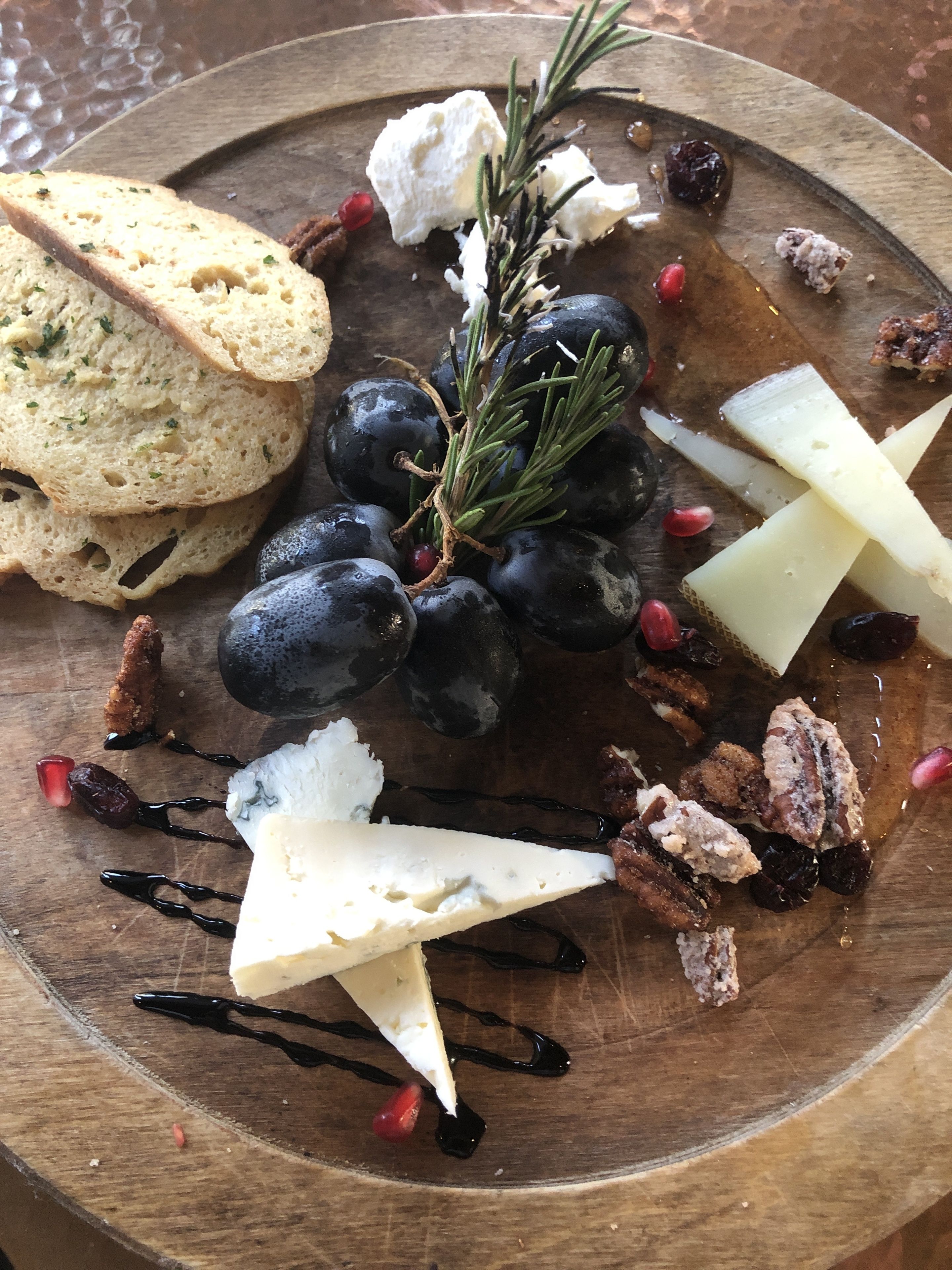 Una tabla de madera con una variedad de quesos, uvas, nueces y pan.