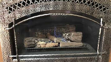 A stone fireplace with a metal grill, surrounded by a textured stone wall.