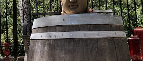 Eine große Holztonnenskulptur mit einem Buddha-Kopf, umgeben von Bäumen und einem Zaun.