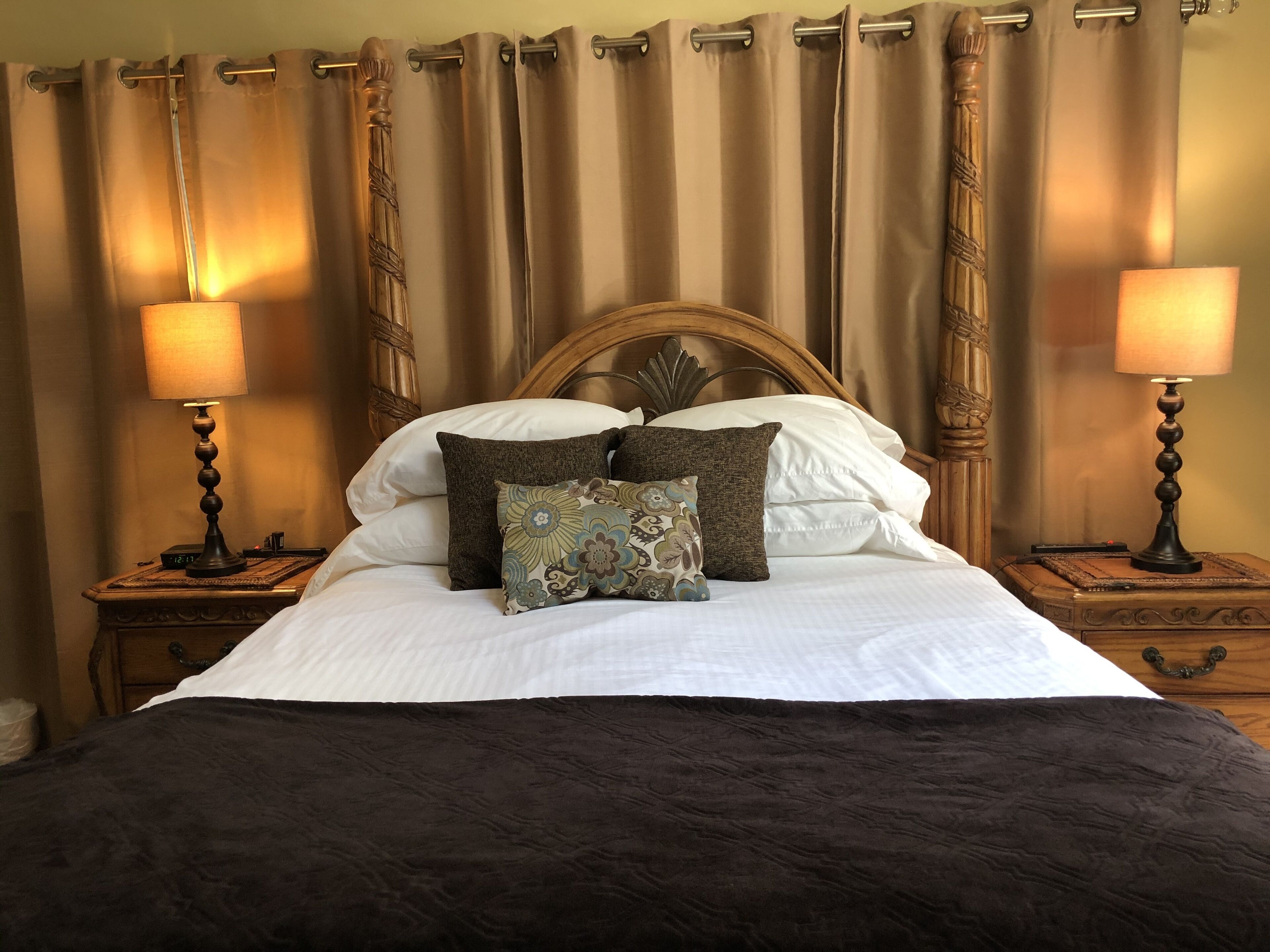 A neatly made bed with a dark blanket, two bedside lamps, and a wooden headboard.