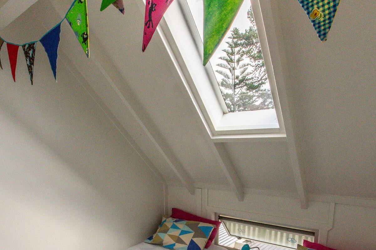 Un dormitorio acogedor en el ático, con dos camas, un tragaluz y guirnaldas coloridas.